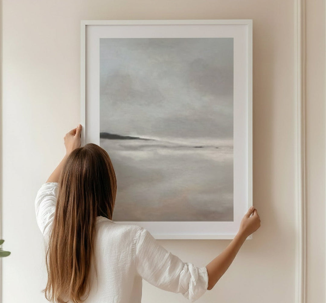 Person hanging a landscape painting on a wall