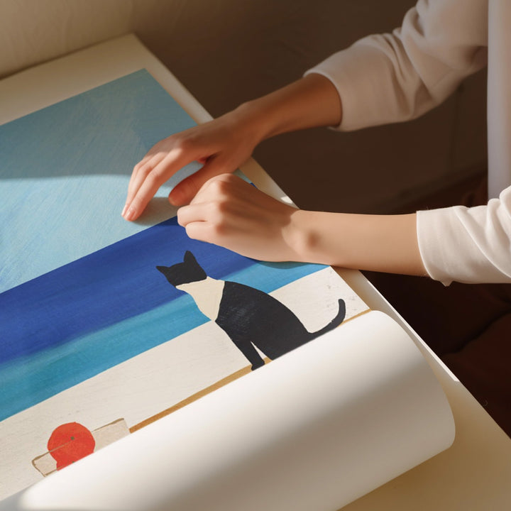Person unrolling a large piece of paper with a cat illustration on a table.