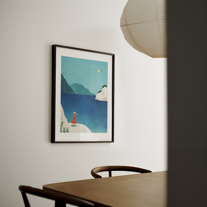 artwork of a person by the sea on a wall above a table.