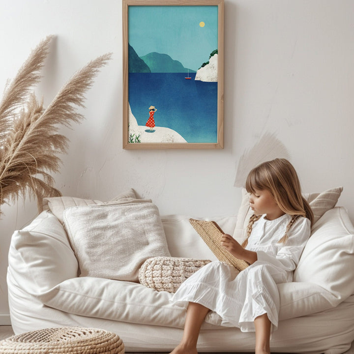 Child reading a book on a white couch with artwork of a beach scene above.