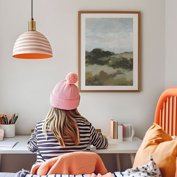 Person wearing a pink beanie sitting at a desk with a painting on the wall.