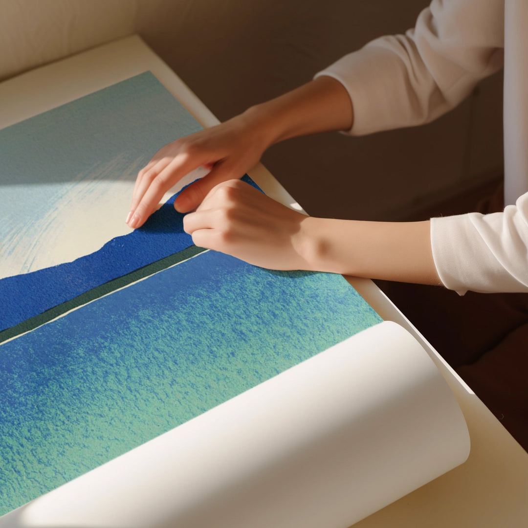 Person unrolling a large piece of paper with a scenic design on a table.