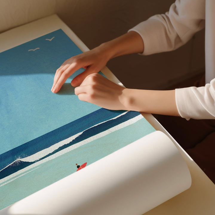 Person rolling out a large beach scene poster on a table