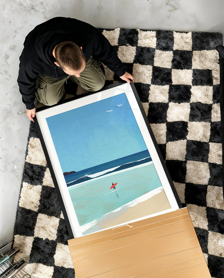Person holding artwork of a beach scene on a checkered rug.