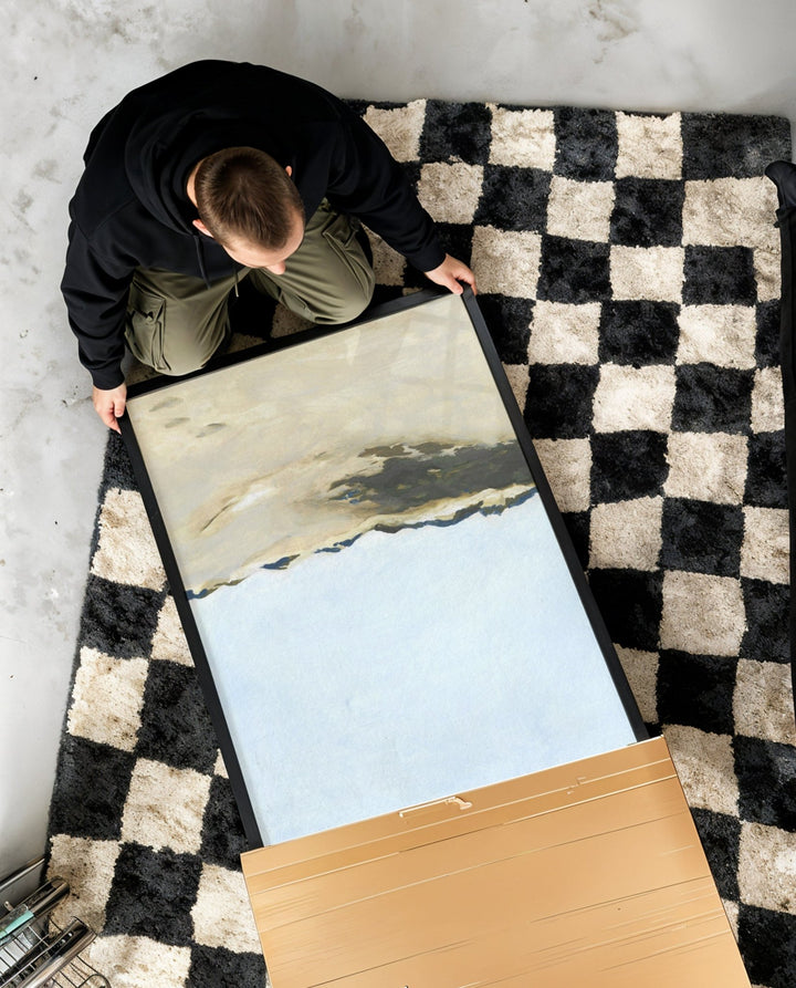 Person unboxing a large artwork on a checkered rug.