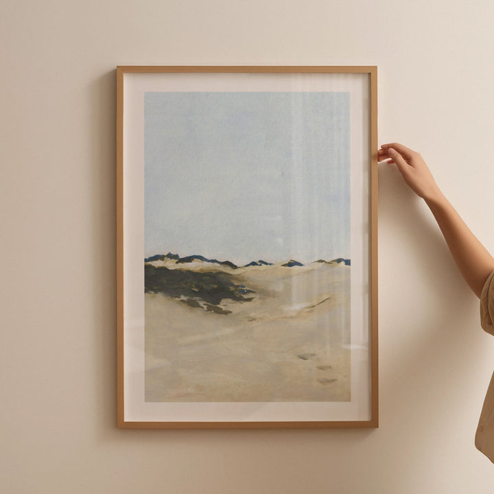 Landscape print on a beige wall with a hand adjusting