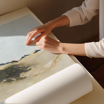 Person unrolling a large piece of paper with a landscape design on a table.