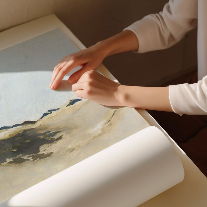 Person unrolling a large piece of paper with a landscape design on a table.
