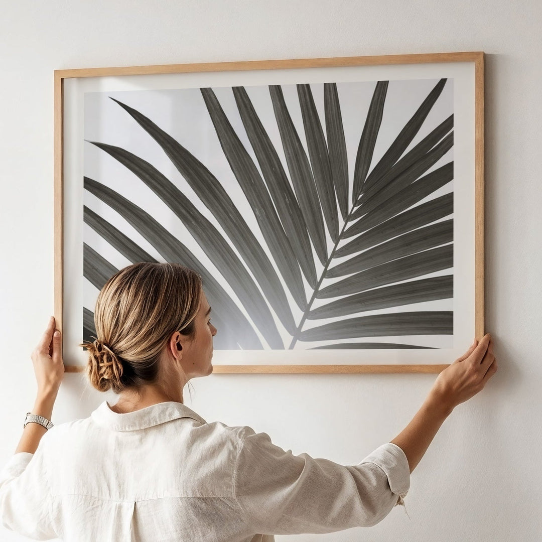 Person hanging a black and white leaf print on a wall