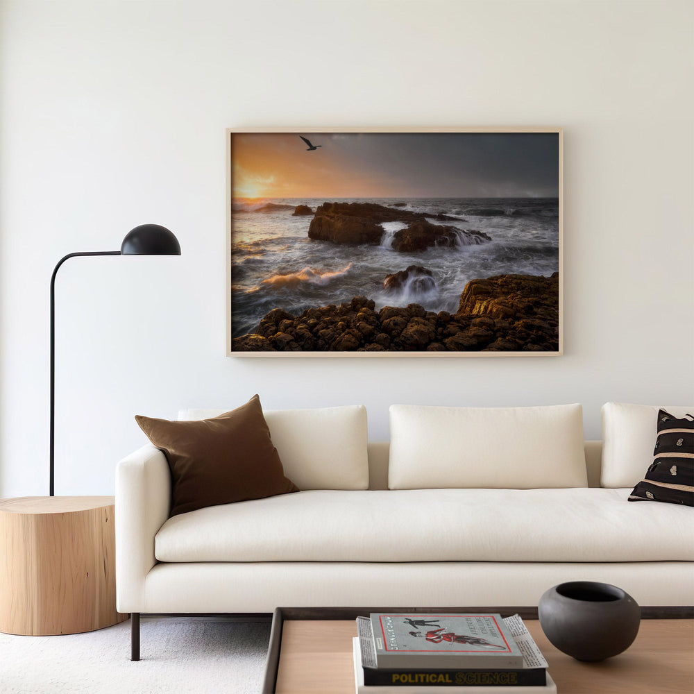 Modern living room with a sofa, lamp, and artwork of a sunset over rocks.