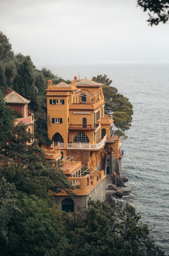 Yellow mansion on a cliff overlooking the ocean with trees around framed