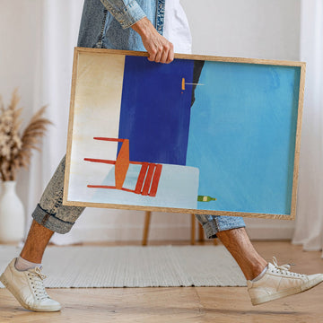 Person holding an abstract art piece with a blue background and red chair.