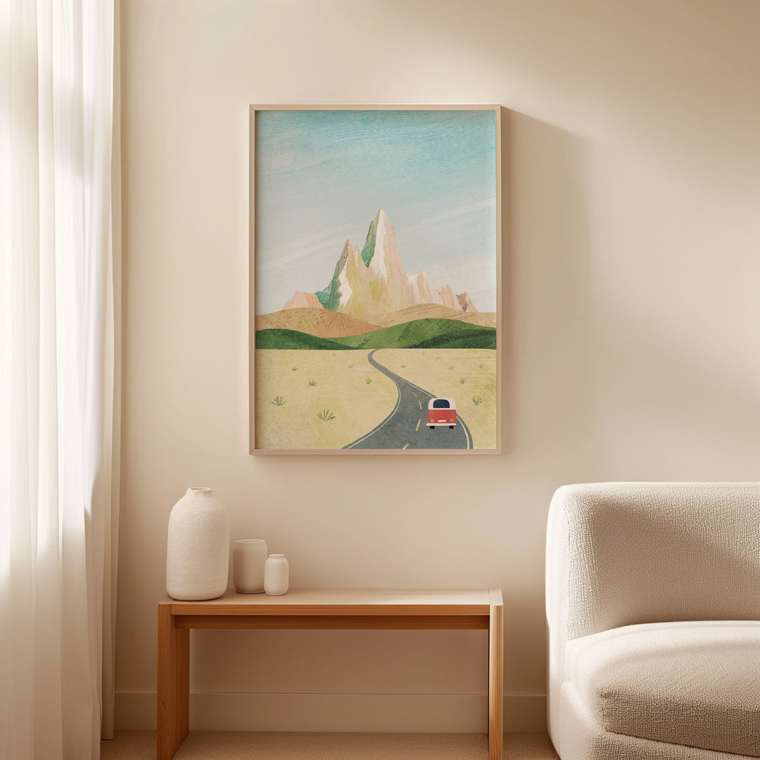 Artwork of a desert scene with a road and car on a beige wall above a wooden side table with decorative items.