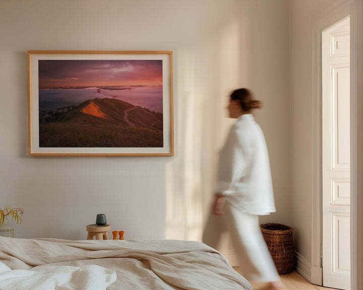 Woman in a white robe walking past a landscape painting in a bedroom.