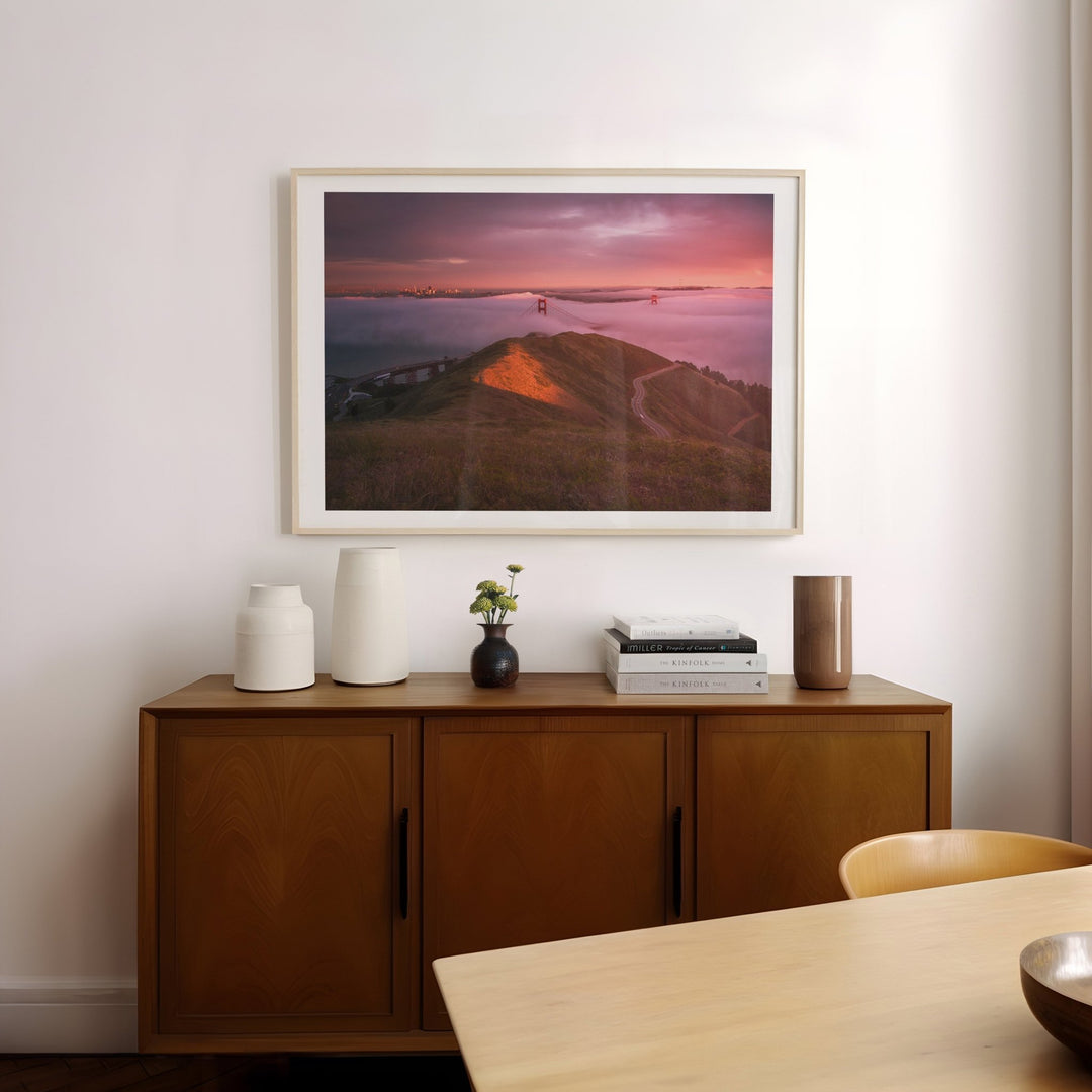 Wooden sideboard with decorative items and a landscape picture on a white wall.