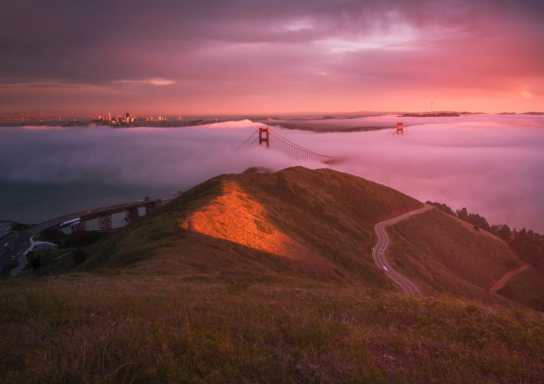 Hilltop view of the Golden Gate Bridge at sunset with a pink and purple sky. framed