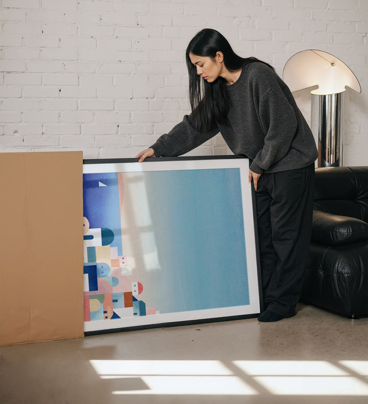Woman holding a large artwork in a living room.