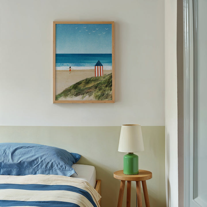 Beach scene art above a bed with a green lamp on a side table.