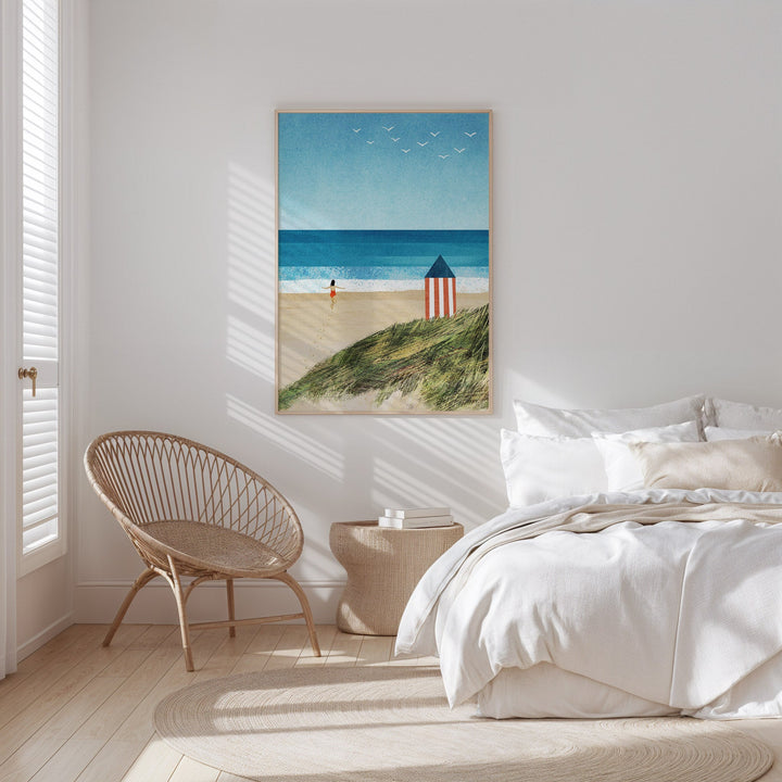 Beach-themed wall art above a bed in a bedroom with a wicker chair and side table.