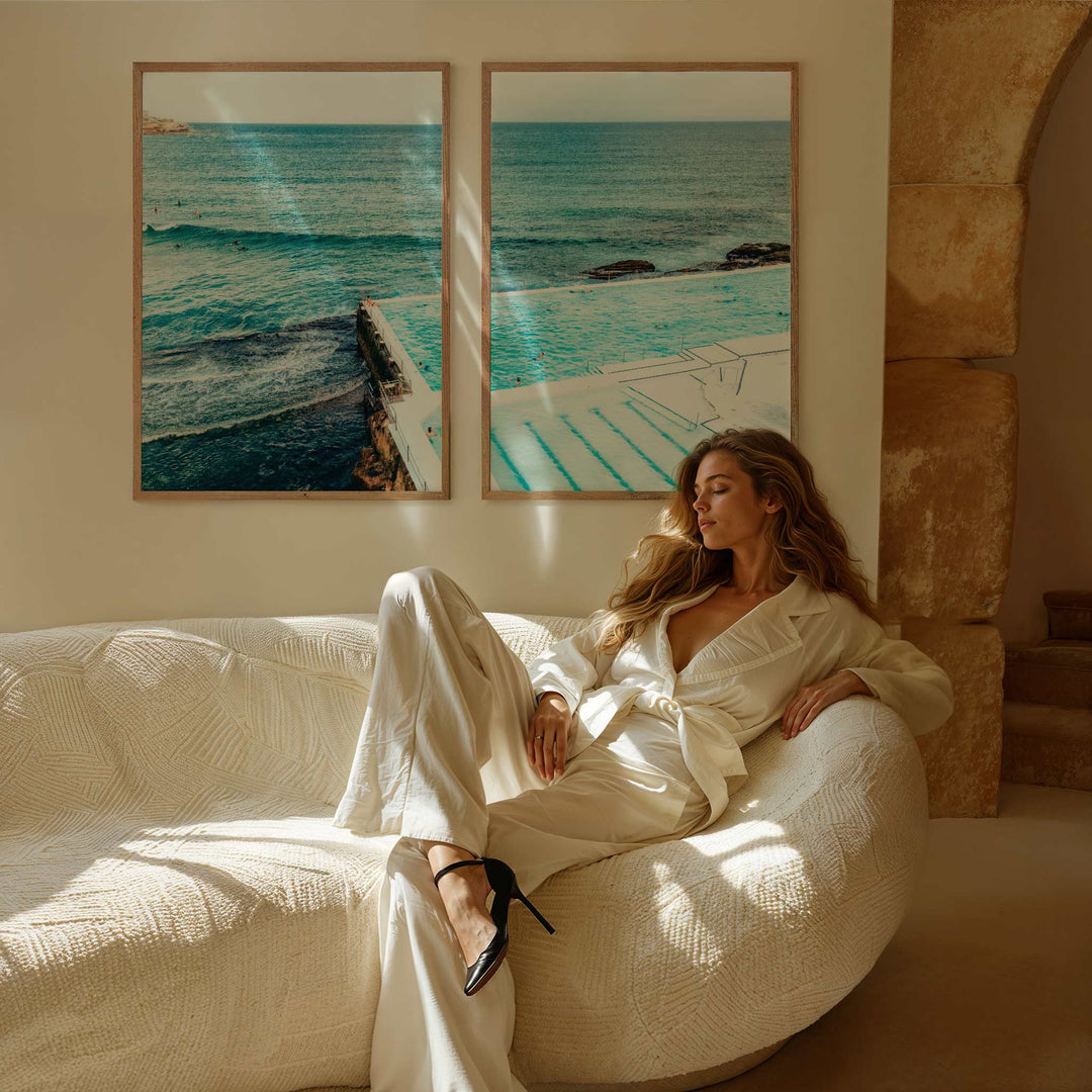 Woman in a white outfit sitting on a white sofa with ocean-themed artwork on the wall.