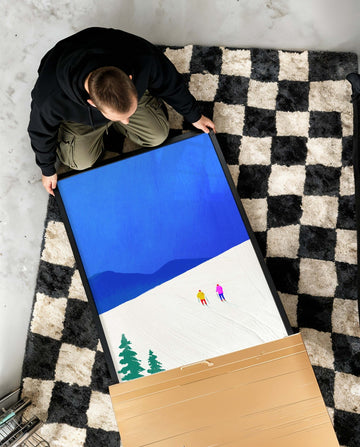 Person unboxing artwork on a checkered floor
