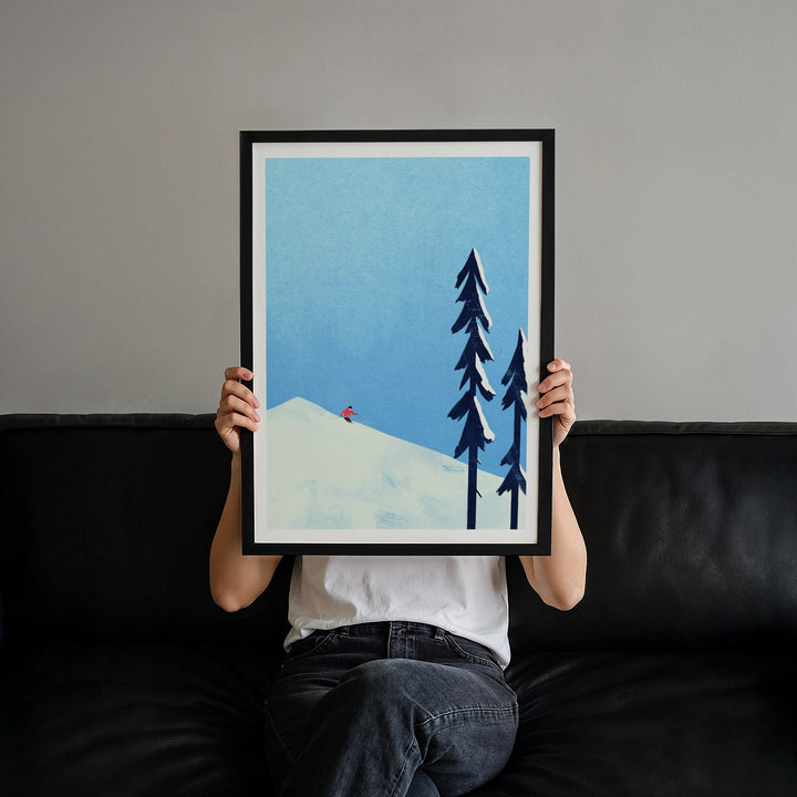 Person holding an artwork of a snowy landscape with trees against a gray wall.