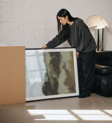 Woman holding a large painting in a living room.