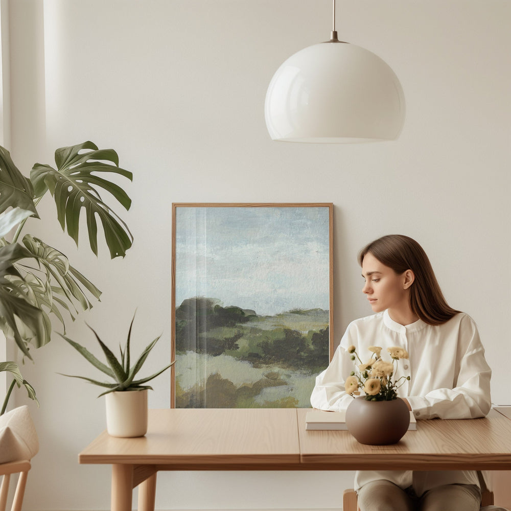 Woman sitting at a table with a scenic painting and plants in a room.