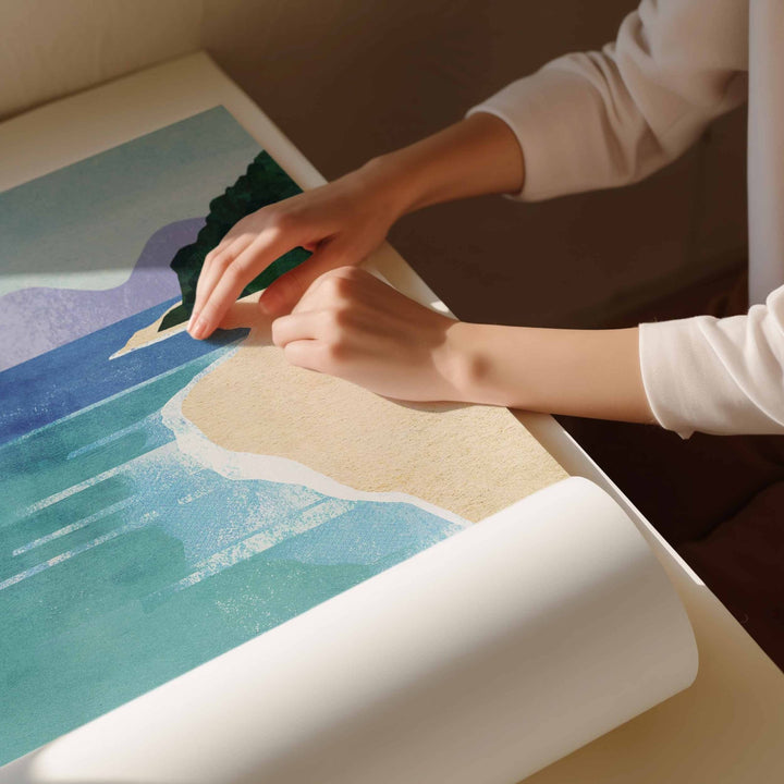 Person unrolling a beach-themed artwork on a table