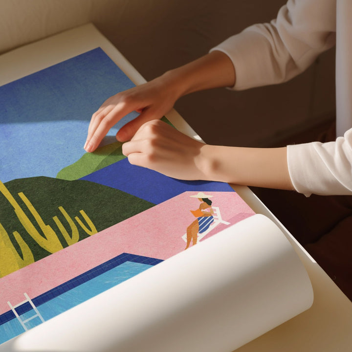 Person rolling out a colorful poster of a scenic design on a table.