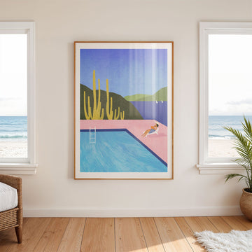 Artwork of a pool scene with a beach view on a wall in a room with windows.