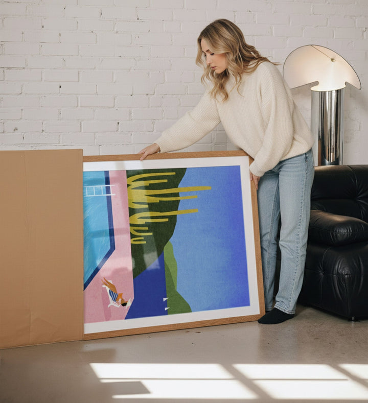 Woman holding an abstract painting in a room with a white brick wall and black leather sofa.