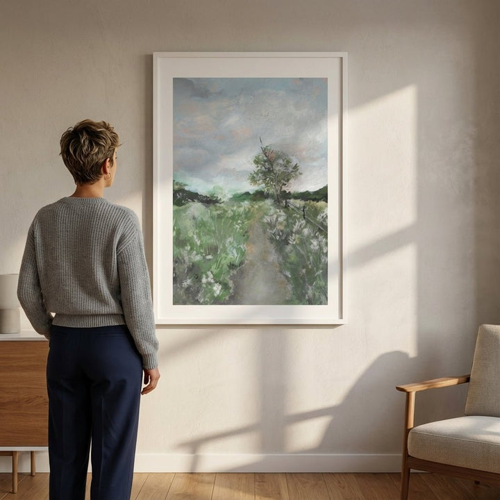 Person standing in a room looking at a landscape painting on the wall.