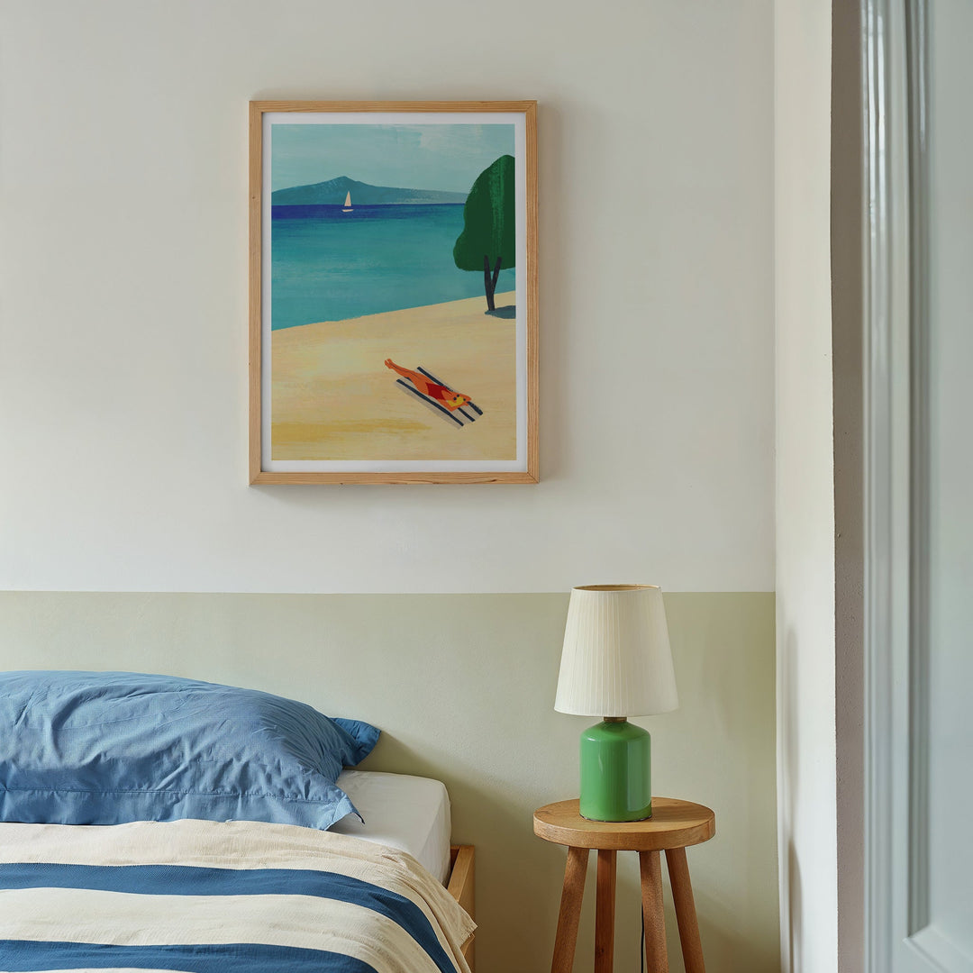 Artwork of a beach scene above a bed with a lamp on a side table.