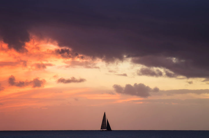 Sailboat on the horizon with a vibrant sunset sky framed