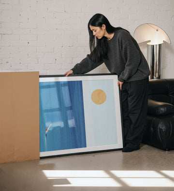 Woman holding an artwork in a living room.