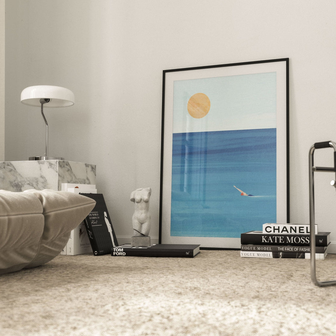 Artwork of a sun and ocean scene on a shelf with books in a room.