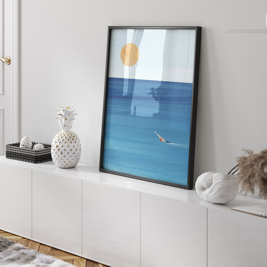 Artwork of a blue ocean scene with a gold sun on a white wall.