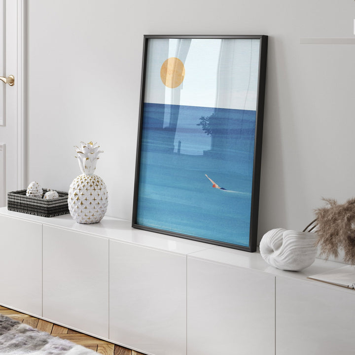 Artwork of a blue ocean scene with a gold sun on a white wall.