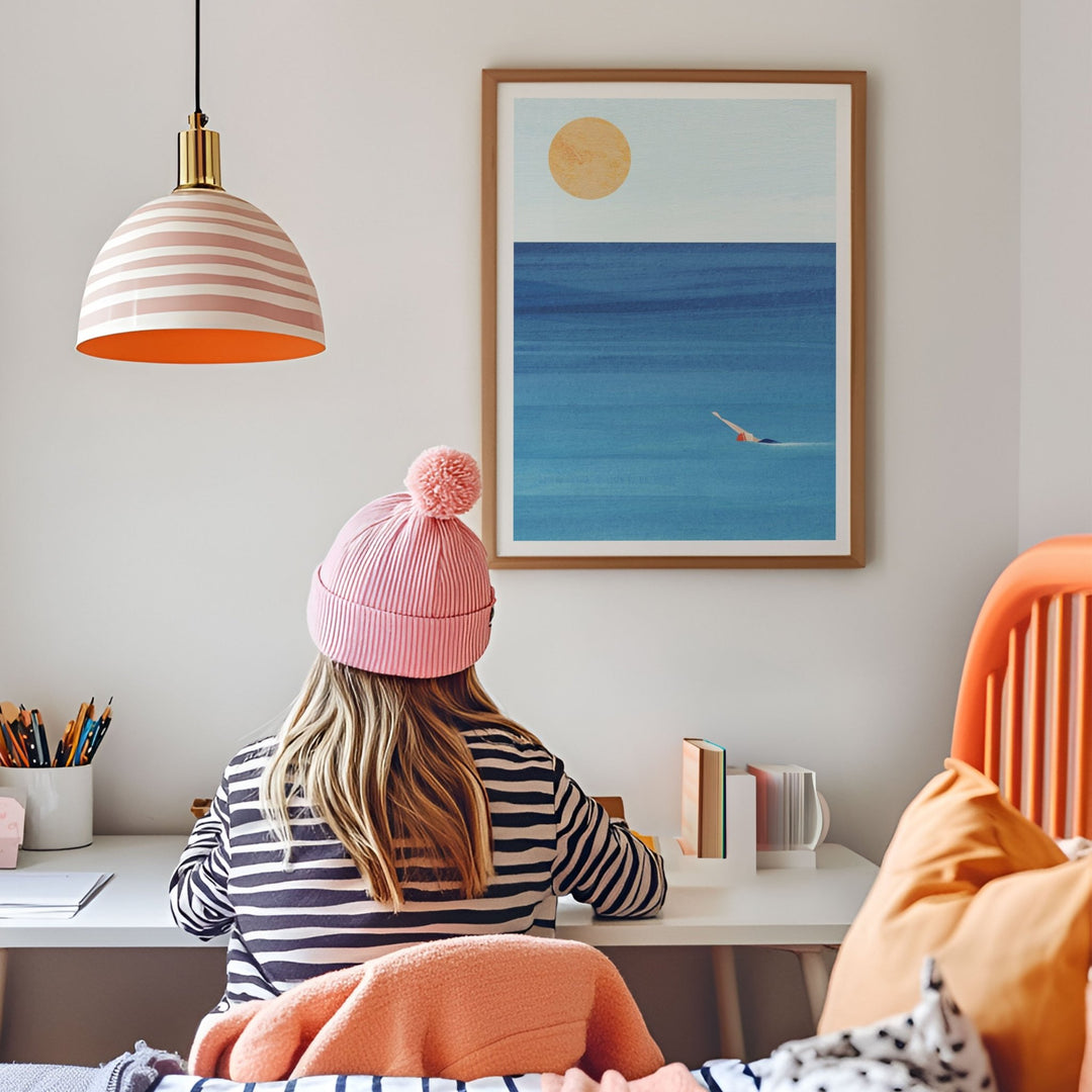 Person wearing a pink beanie sitting at a desk with artwork of a beach scene on the wall.