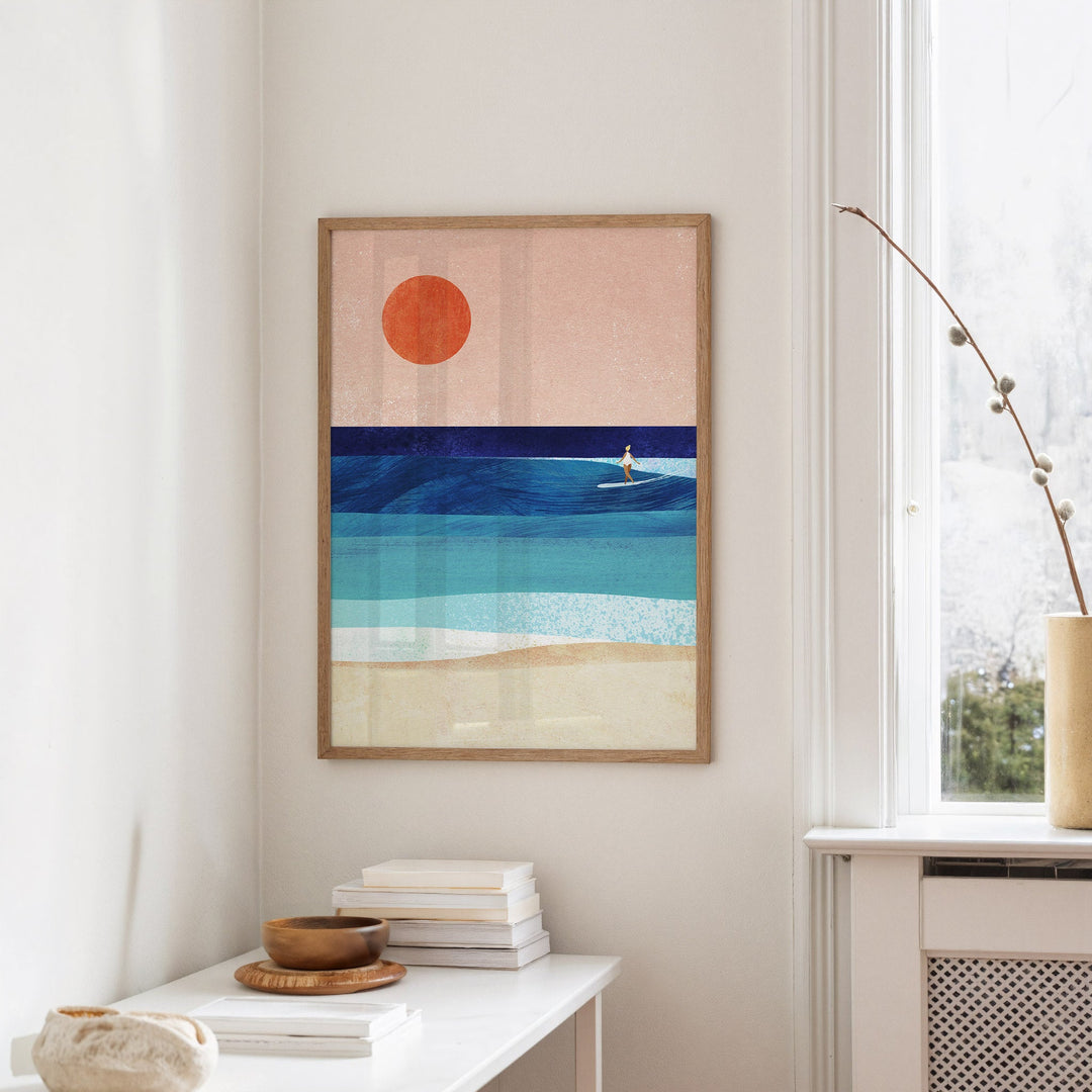 Artwork of a beach scene with a red sun and blue water, displayed on a wall.