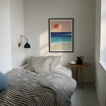 Modern bedroom with striped bedding, side table, and abstract wall art.