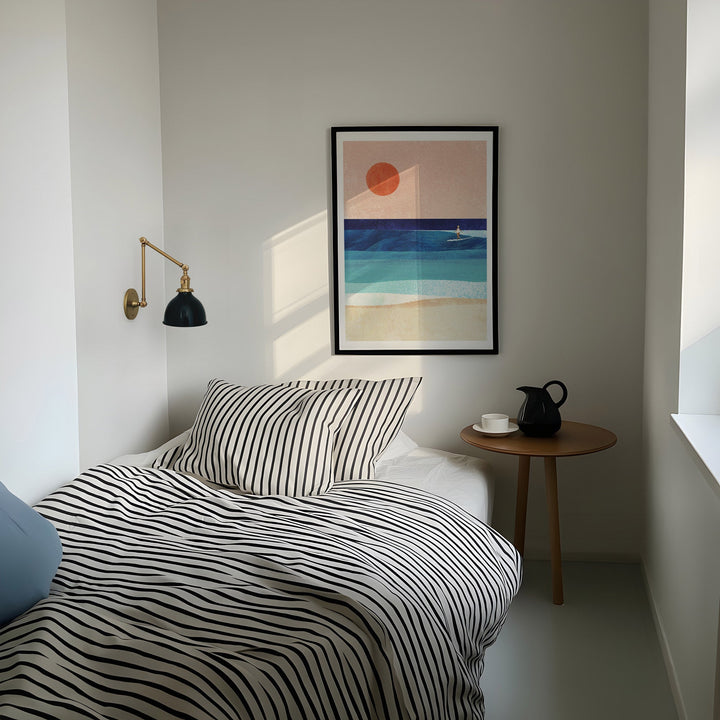 Modern bedroom with striped bedding, side table, and abstract wall art.