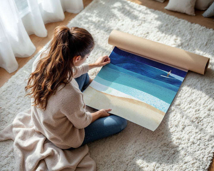 Woman unrolling a large beach scene painting on a carpeted floor.