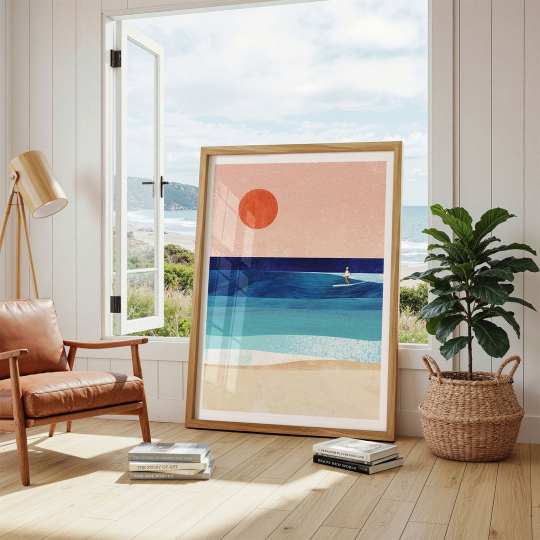 Abstract beach scene art in a room with a chair, plant, and window view.
