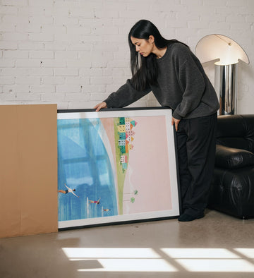 Person holding an artwork in a living room setting