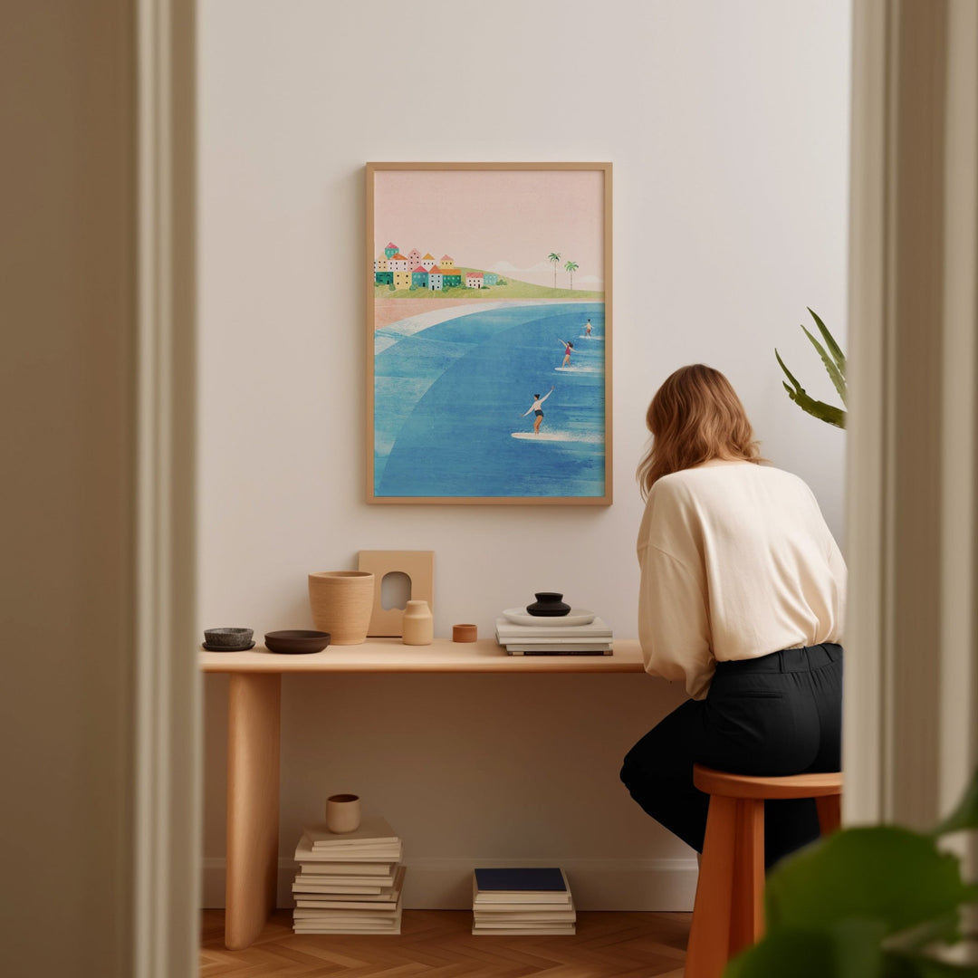 Person sitting at a desk in a room with an artwork of a beach scene on the wall.