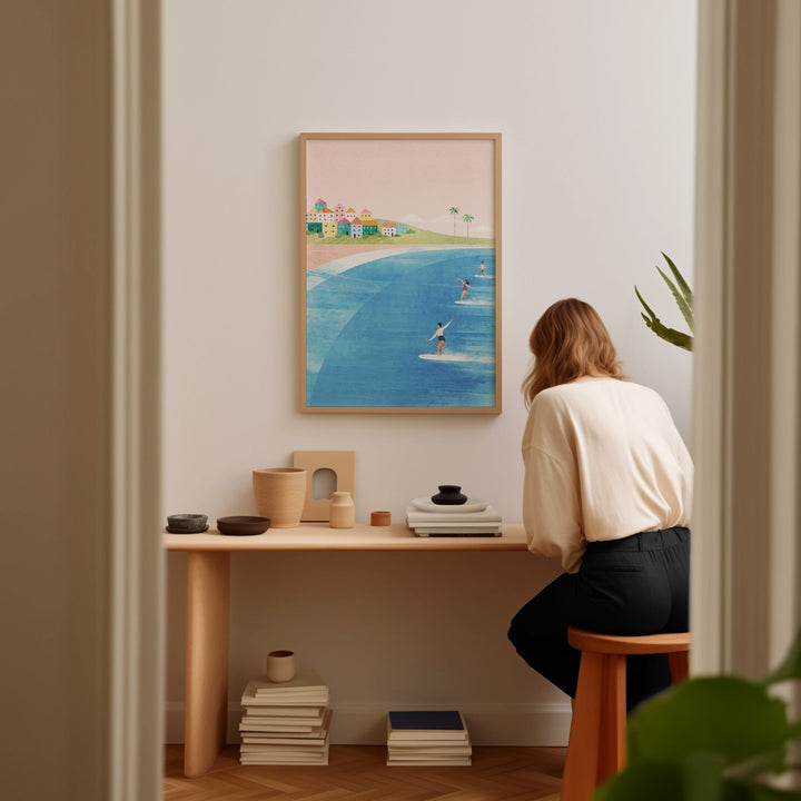 Person sitting at a desk in a room with an artwork of a beach scene on the wall.