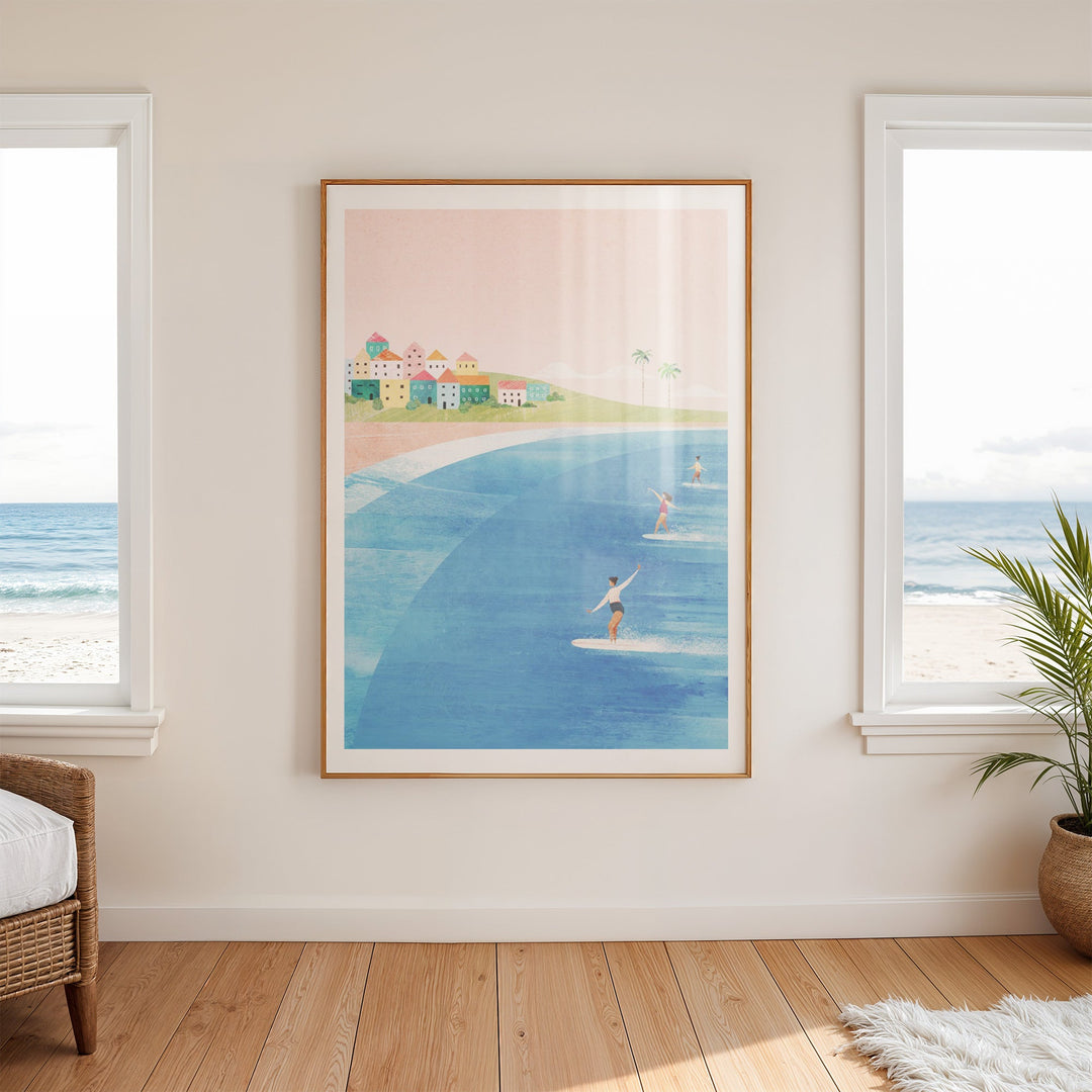 Artwork of a beach scene with people on a boardwalk and houses, hanging on a wall in a room with windows and a plant.