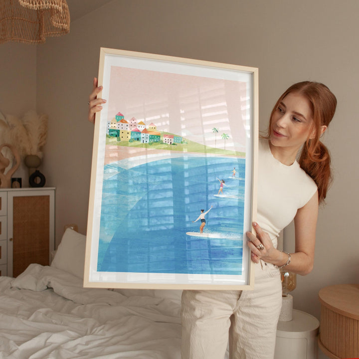 Woman holding an artwork of a coastal scene with people on surfboards.
